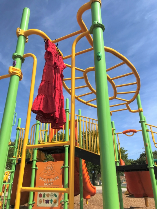 A red tiered dress on a black clothes hanger hanging off of the monkey bars at a play structure.