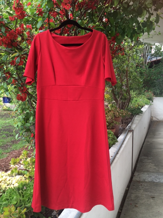 A red sleeved dress on a black clothes hanger hanging from a tree in a courtyard
