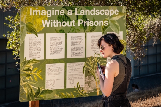 2020-2021 IAS Pathways Fellow, Chloe Murr is pictured standing next to a green sign with white text that reads 'Imagine a Landscape Without Prisons'